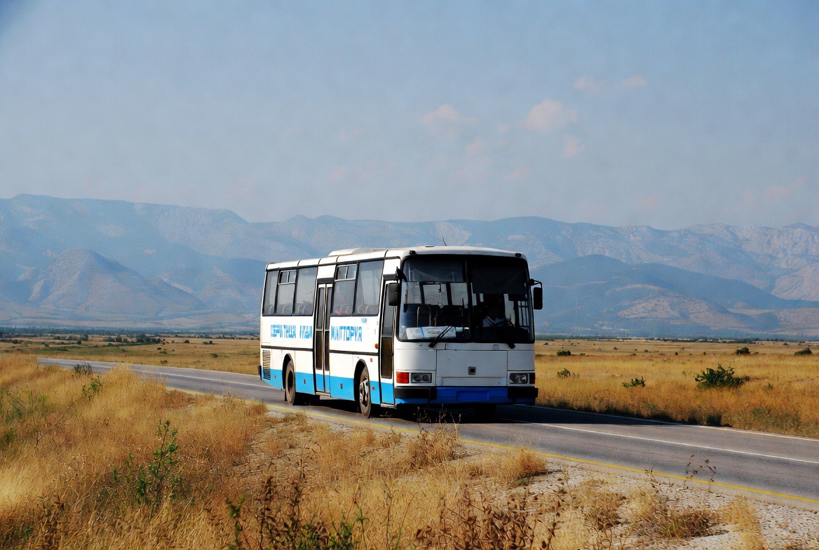 Bulgarian intercity bus on a rural road with mountains in the background, the backbone of Bulgaria budget travel